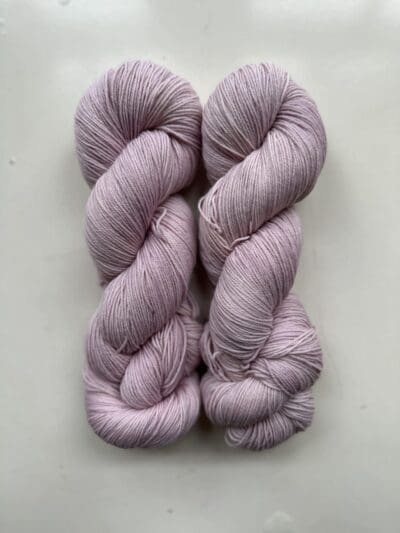 Purple Colorway: Light Lilac. Length: 437 yds / 400 meters. 100 Grams. Introducing Light Lilac 4-ply sock yarn, a naturally dyed blend of 75% Superwash Merino and 25% nylon. This Peru-origin yarn is hand-dyed using plant-based dyes, resulting in an eco-friendly option. Perfect for knitting or crocheting projects. Care Instructions: Hand wash in cold water with a gentle detergent made specifically for washing wool and other fine fibers, or a PH-neutral, dye free detergent. Lay flat to dry. <strong>While our team hand-dyes each skein with the utmost care, natural dyes results can vary based on plant materials and fibers. Please be aware that variations in color and appearance may vary from the display image.  </strong>  